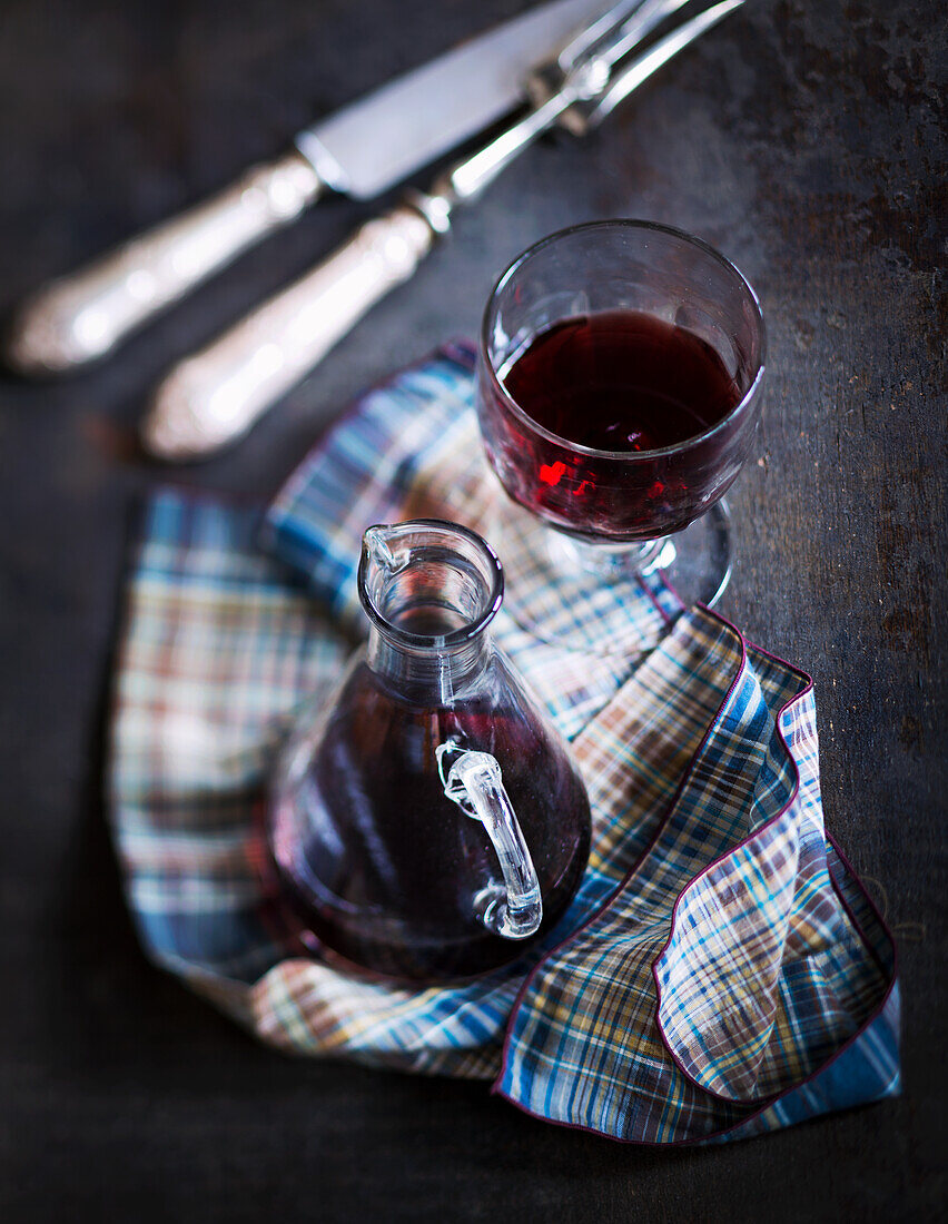 Red wine in a glass and carafe on a checkered cloth next to cutlery