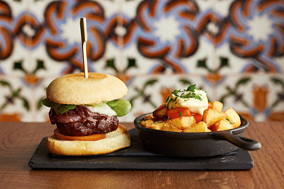 A cheese burger with red onion relish, fried potatoes and aioli in a skillet