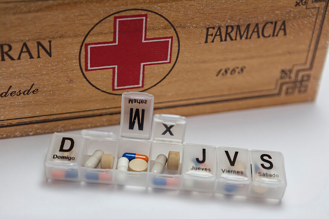 Pills in a pill organizer next to an old wooden kit