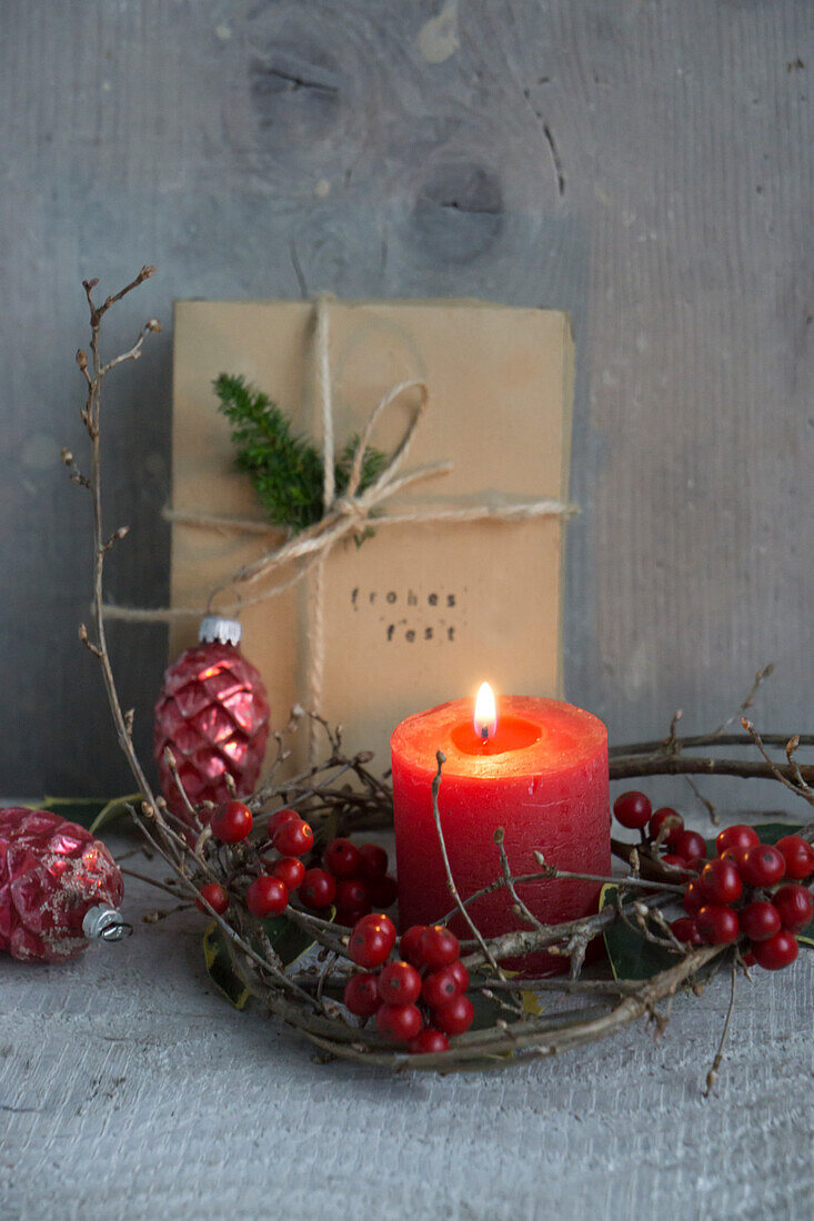 Candle in a wreath of holly berries with wrapped Christmas gift