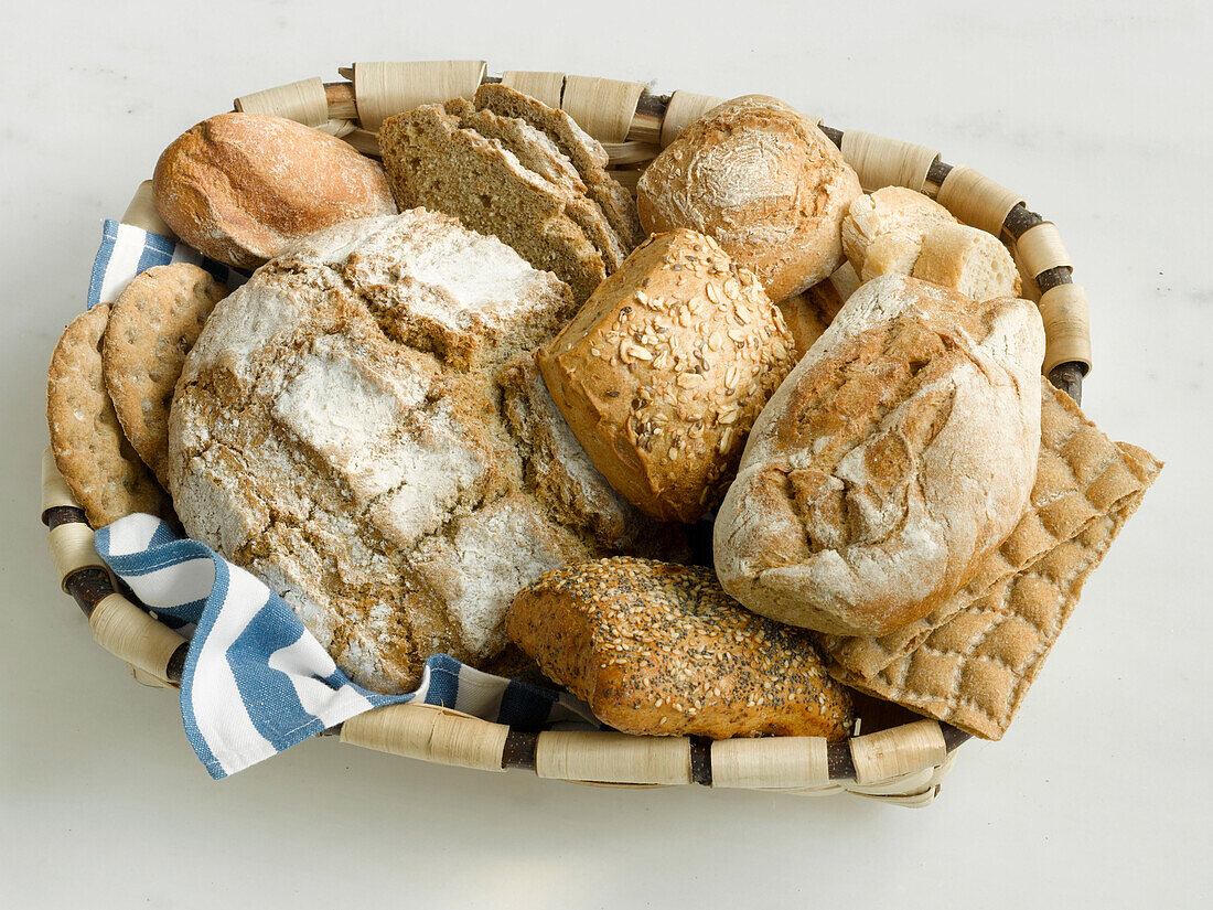 Ein Körbchen mit verschiedenen Sorten Brot und Brötchen auf hellem Untergrund