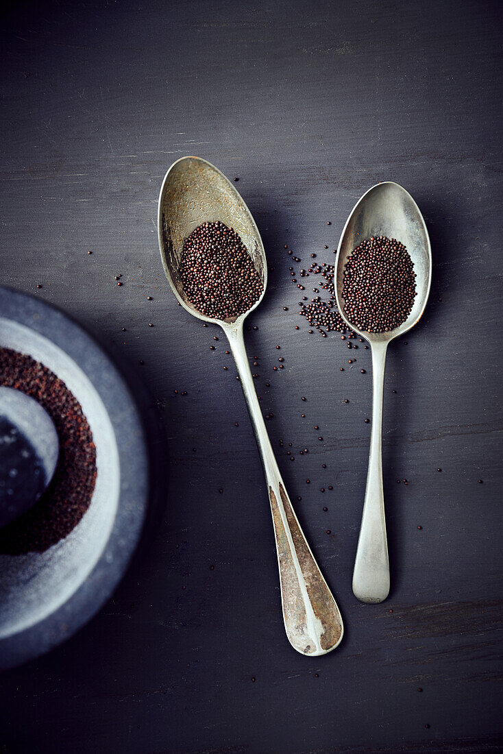 Brown mustard seeds in a mortar and on two spoons