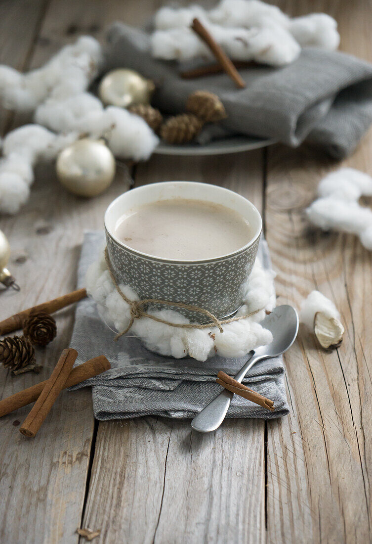 A cup of coffee with milk, decorated with a cotton wreath, napkin, cinnamon sticks and larch cones