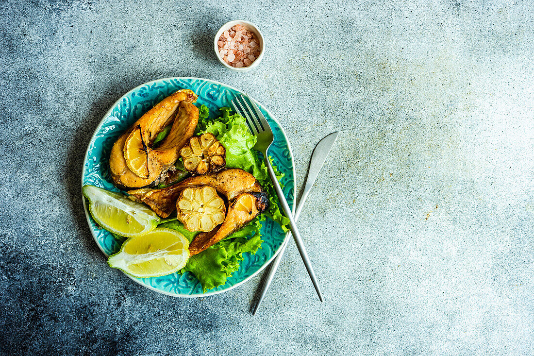 Grilled trout steaks with garlic and salad on a ceramic plate