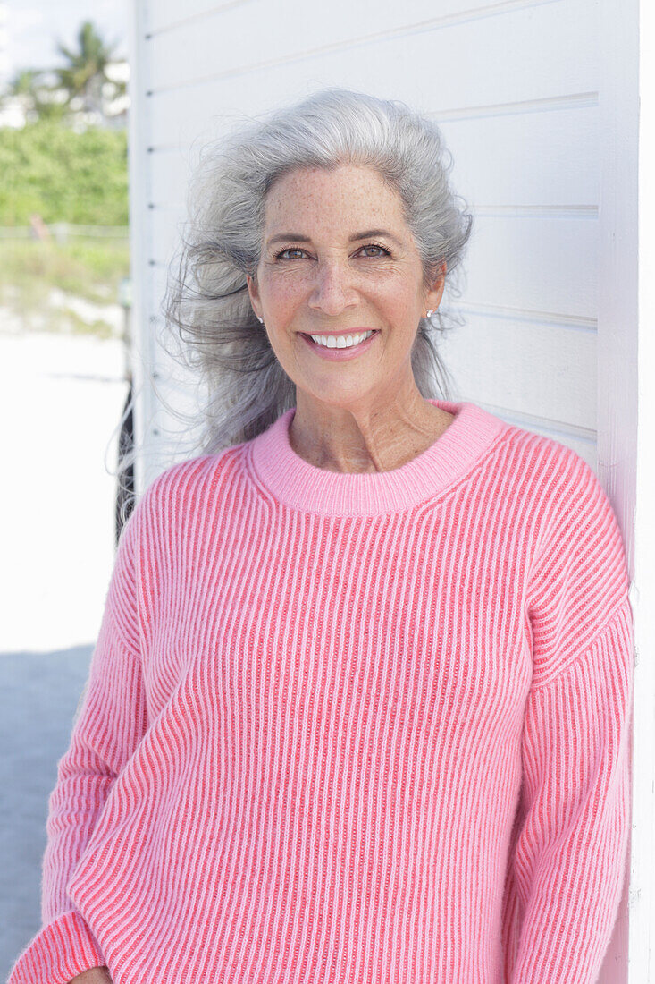 A grey-haired woman wearing a pink jumper on the beach