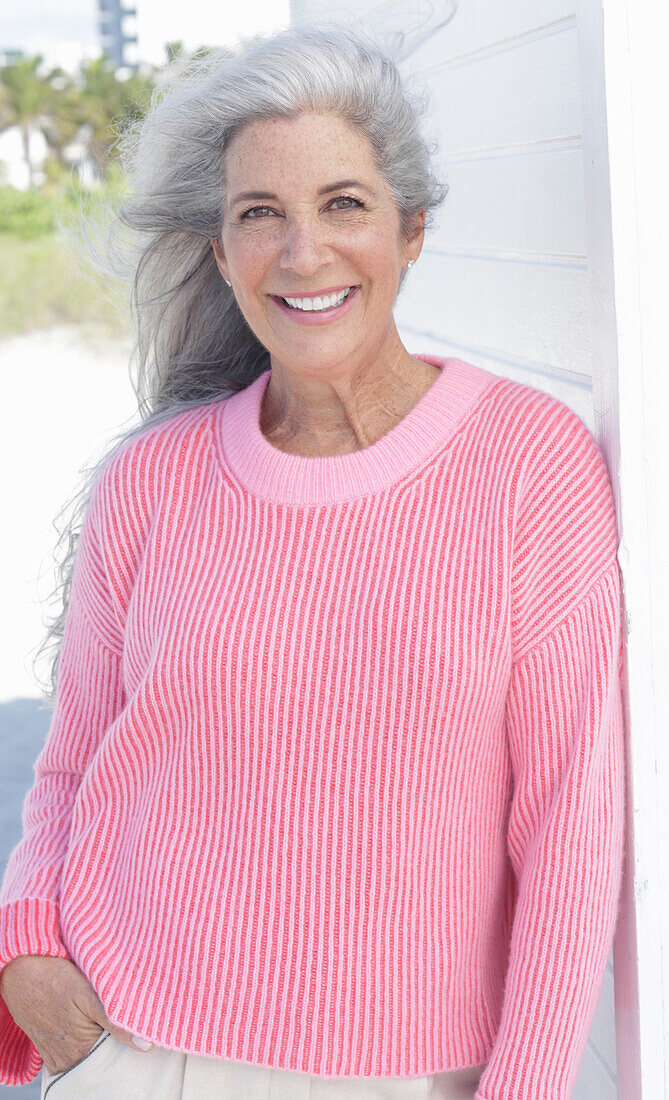 Grauhaarige Frau in pinkfarbenem Pullover am Strand