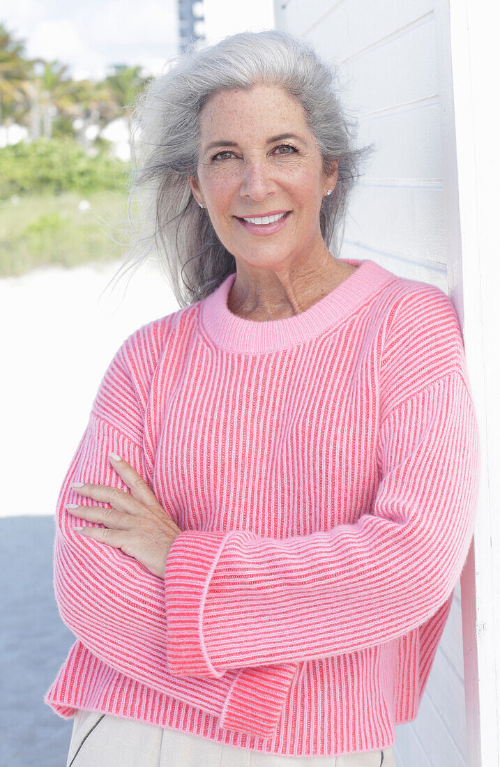 Gray haired woman in a pink sweater on the beach