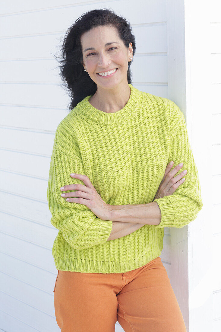 Mature, dark-haired woman in a green and yellow knit sweater and orange pants