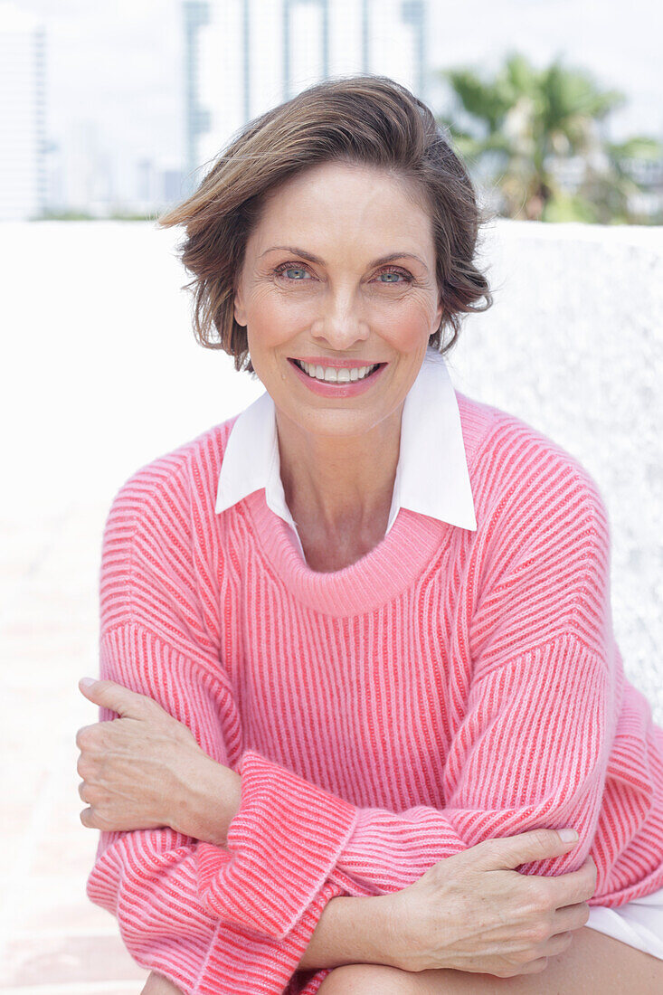 A woman wearing a pink jumper and a white shirt on the beach