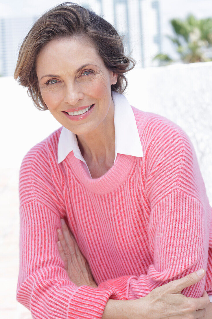 Frau in pinkfarbenem Pullover und weißem Hemd am Strand