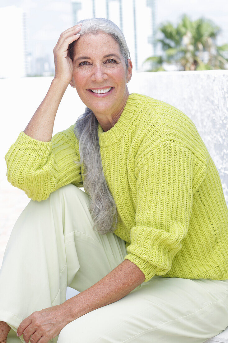 Grauhaarige Frau in grüngelbem Strickpullover und heller Hose