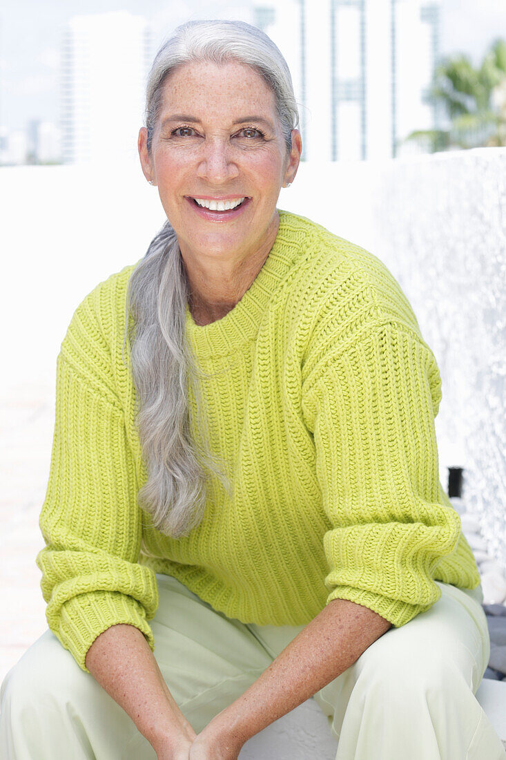 Gray-haired woman in a green-yellow knit sweater and light-colored trousers