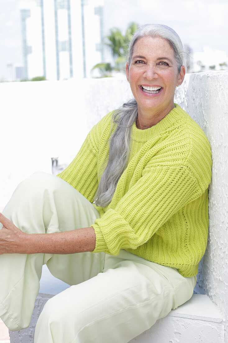 Grauhaarige Frau in grüngelbem Strickpullover und heller Hose