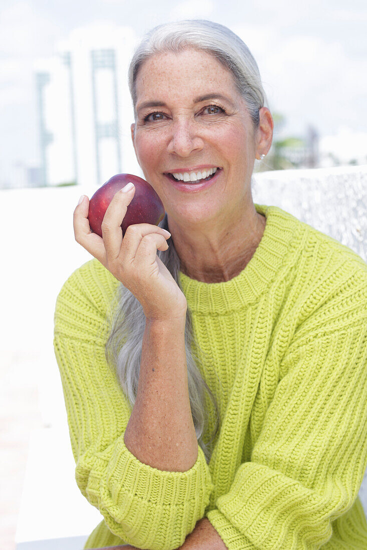 Gray-haired woman with an apple in a green and yellow knit sweater