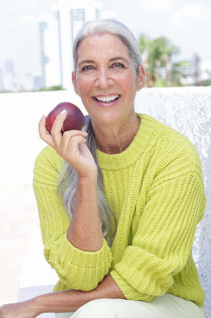 Gray-haired woman with an apple in a green and yellow knit sweater