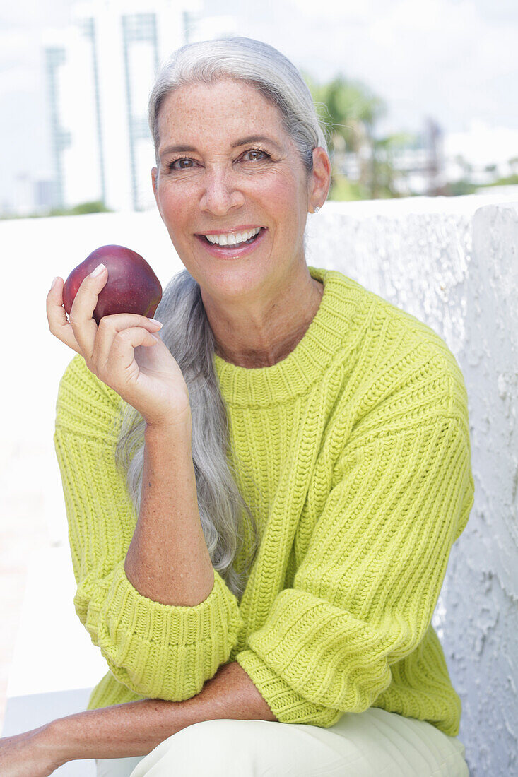 Gray-haired woman with an apple in a green and yellow knit sweater