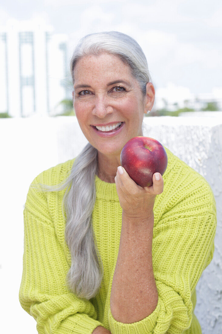 Grauhaarige Frau mit einem Apfel in grüngelbem Strickpullover