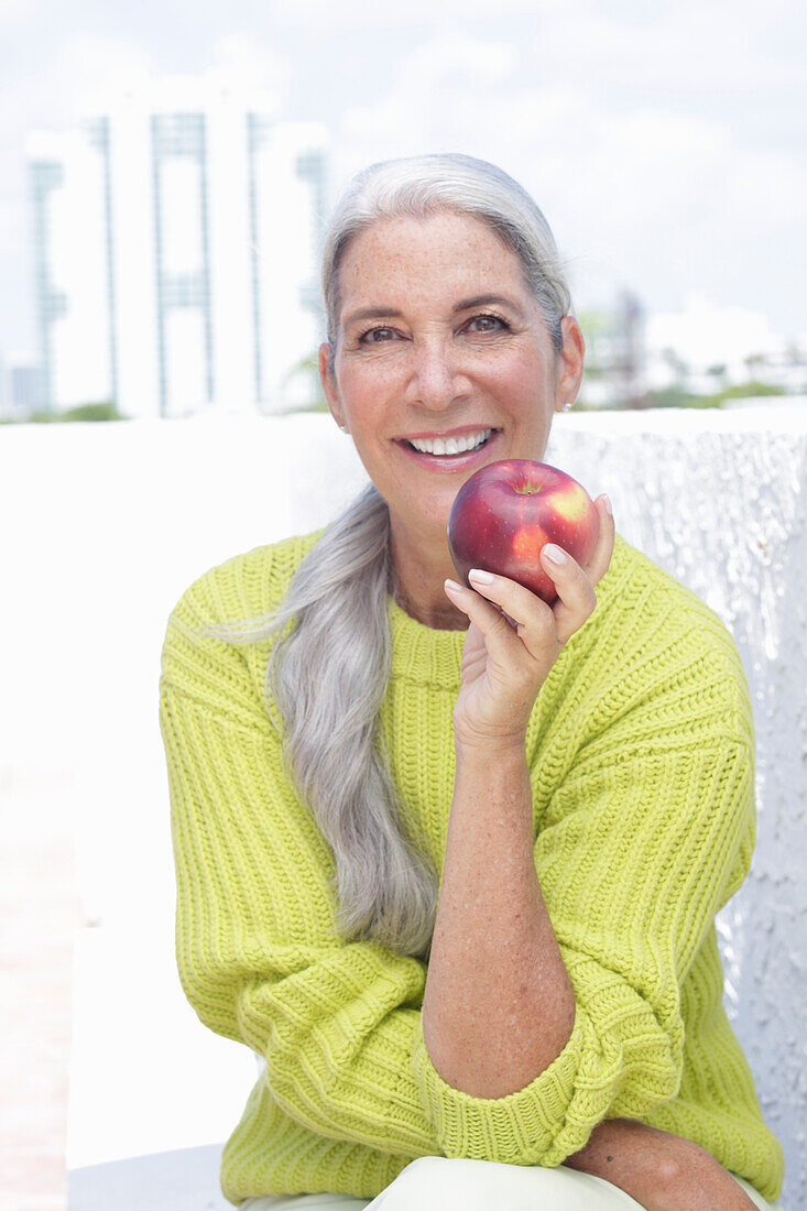 Grauhaarige Frau mit einem Apfel in grüngelbem Strickpullover