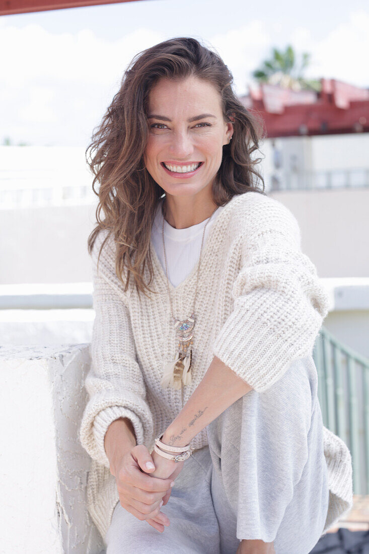 Happy, long-haired woman in light, casual knitted jumper and trousers