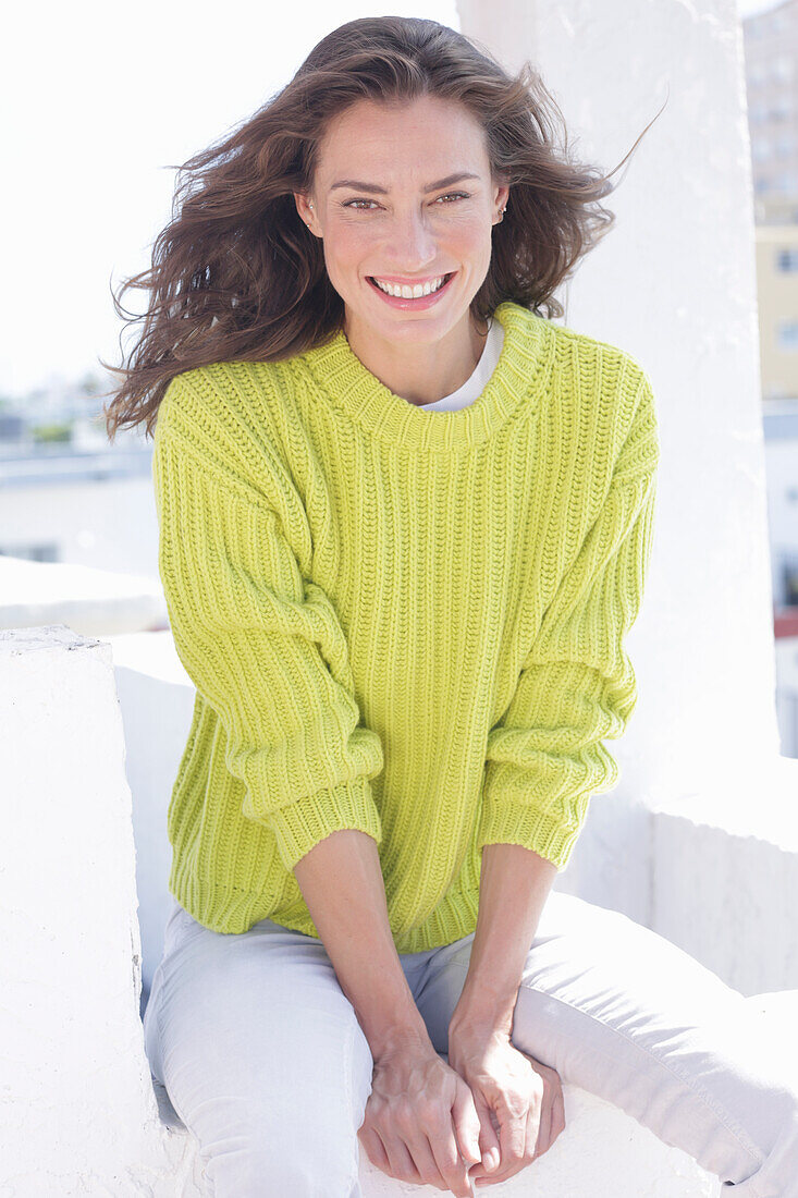 Cheerful longhaired woman in green-yellow knitted jumper and white trousers