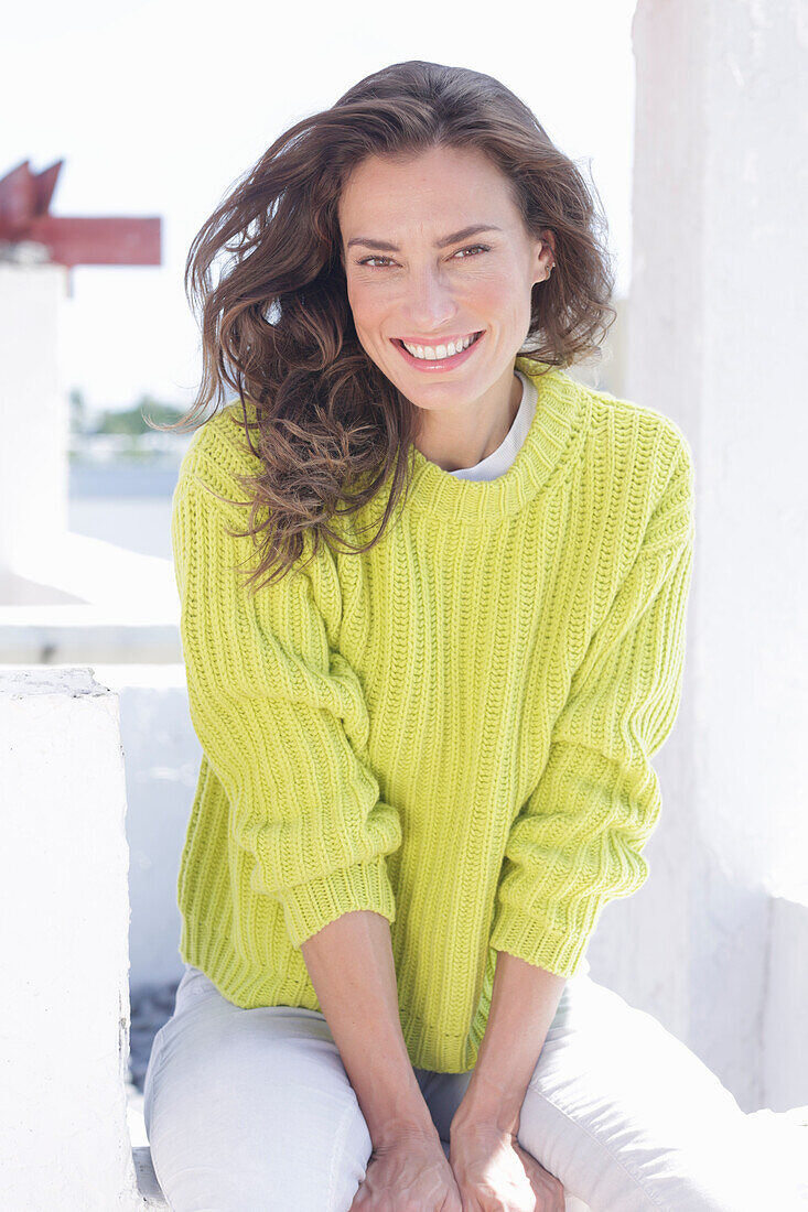Long-haired woman in green-yellow knitted jumper and white trousers