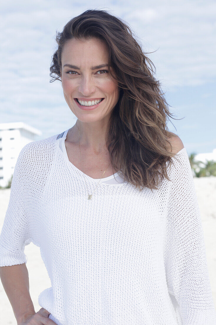 A long-haired woman on the beach wearing a white jumper