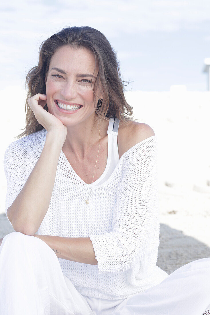 Happy, long-haired woman in white jumper and white trousers on the beach