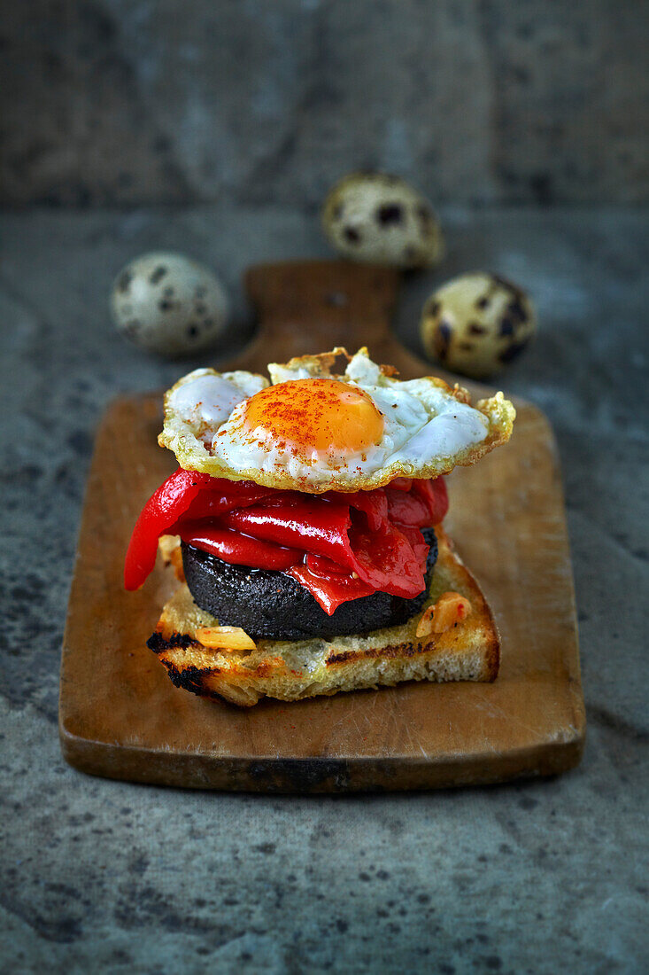 Toasted bread with morcilla (blood sausage), braised peppers, and quail egg