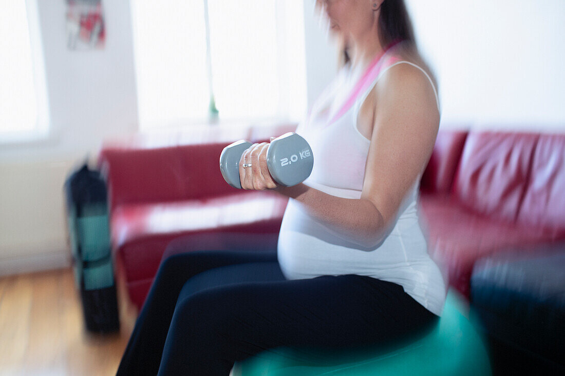 Pregnant woman exercising with dumbbells on fitness ball