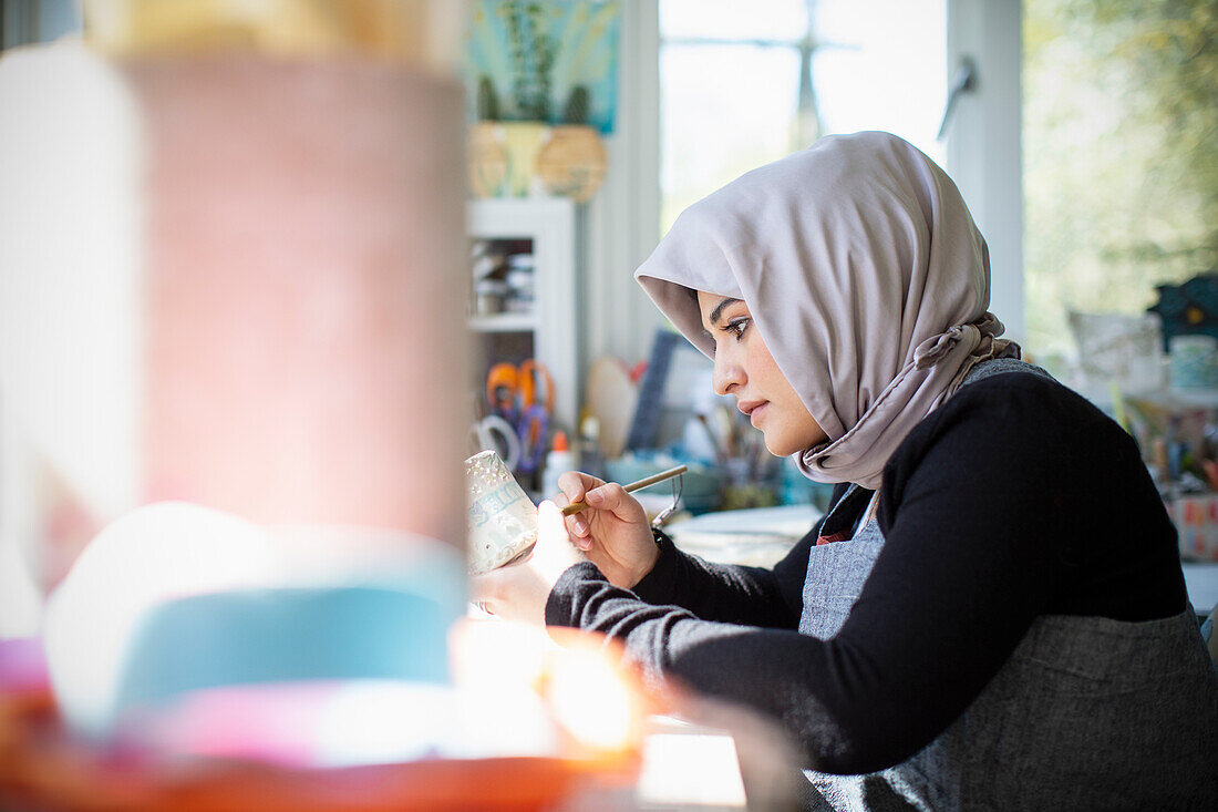 Female artist in hijab painting ceramics in art studio