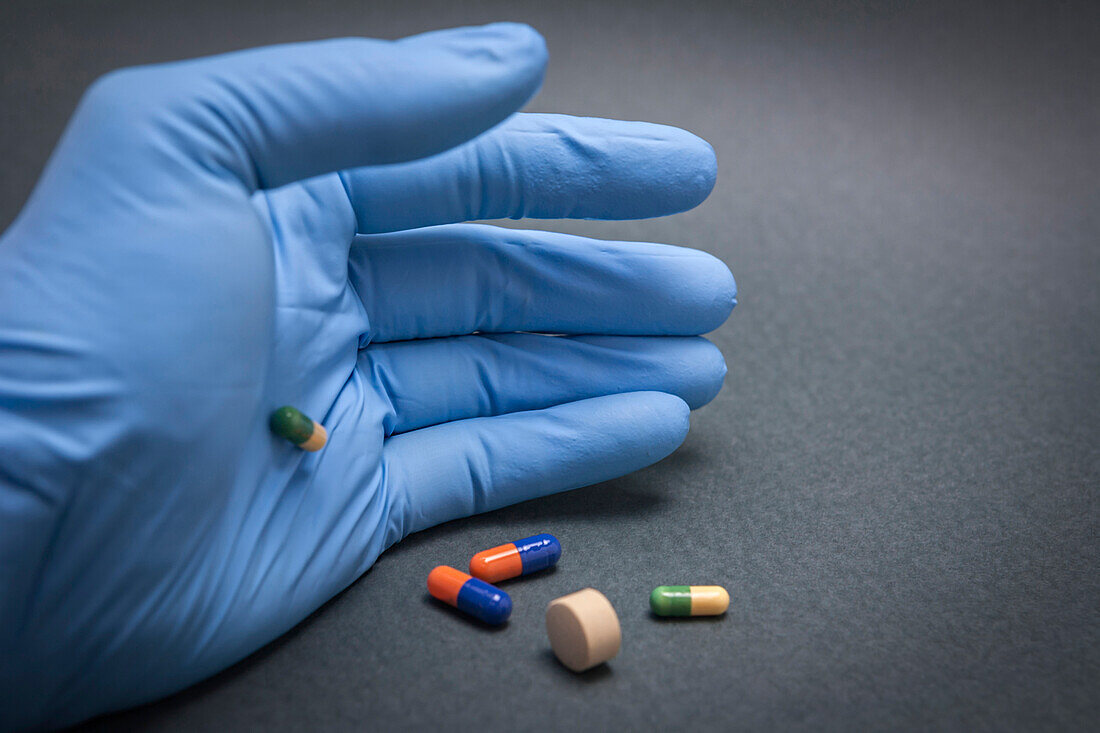 Blue latex gloved hand holding several pills