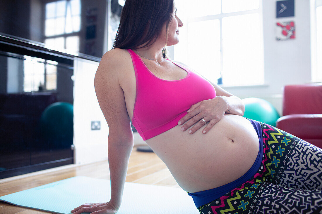 Pregnant woman in sports bra resting on yoga mat at home
