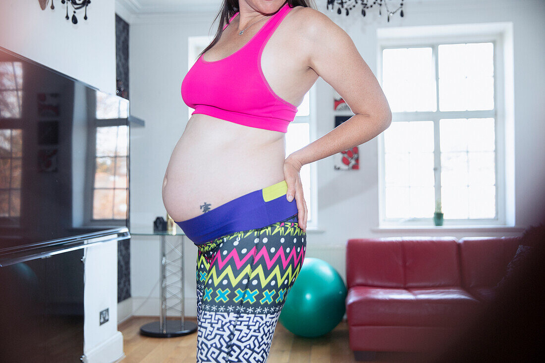 Pregnant woman in sports bra and leggings exercising at home