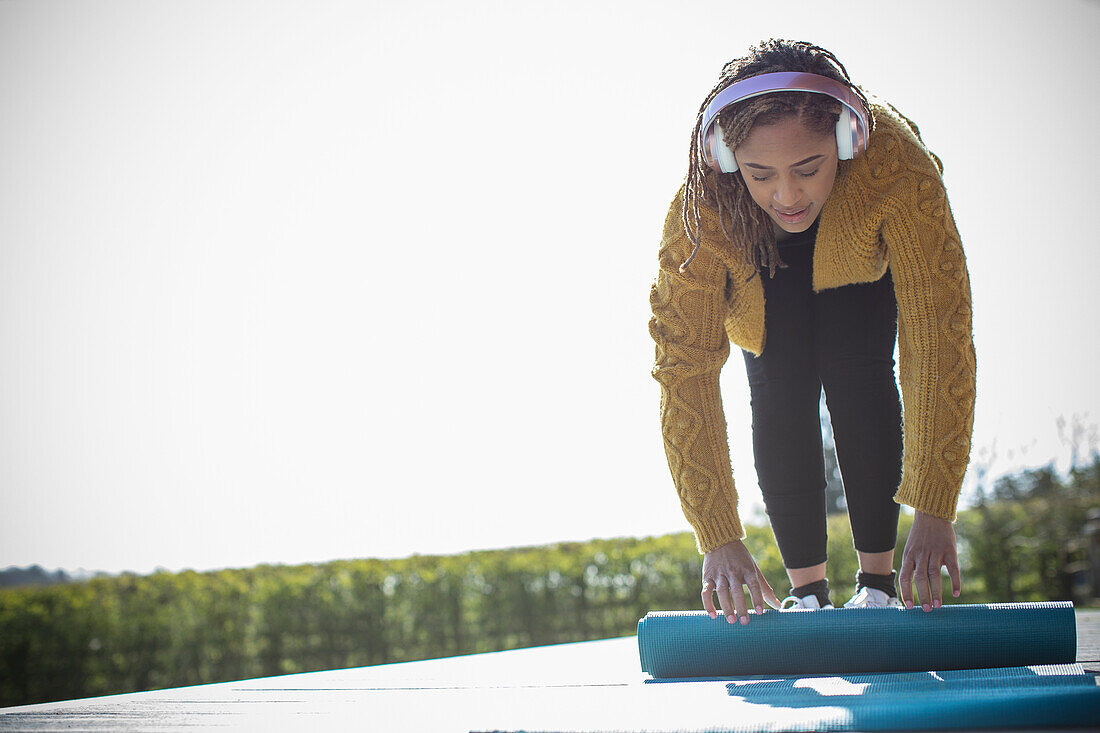 Young woman with headphones rolling up yoga mat on patio