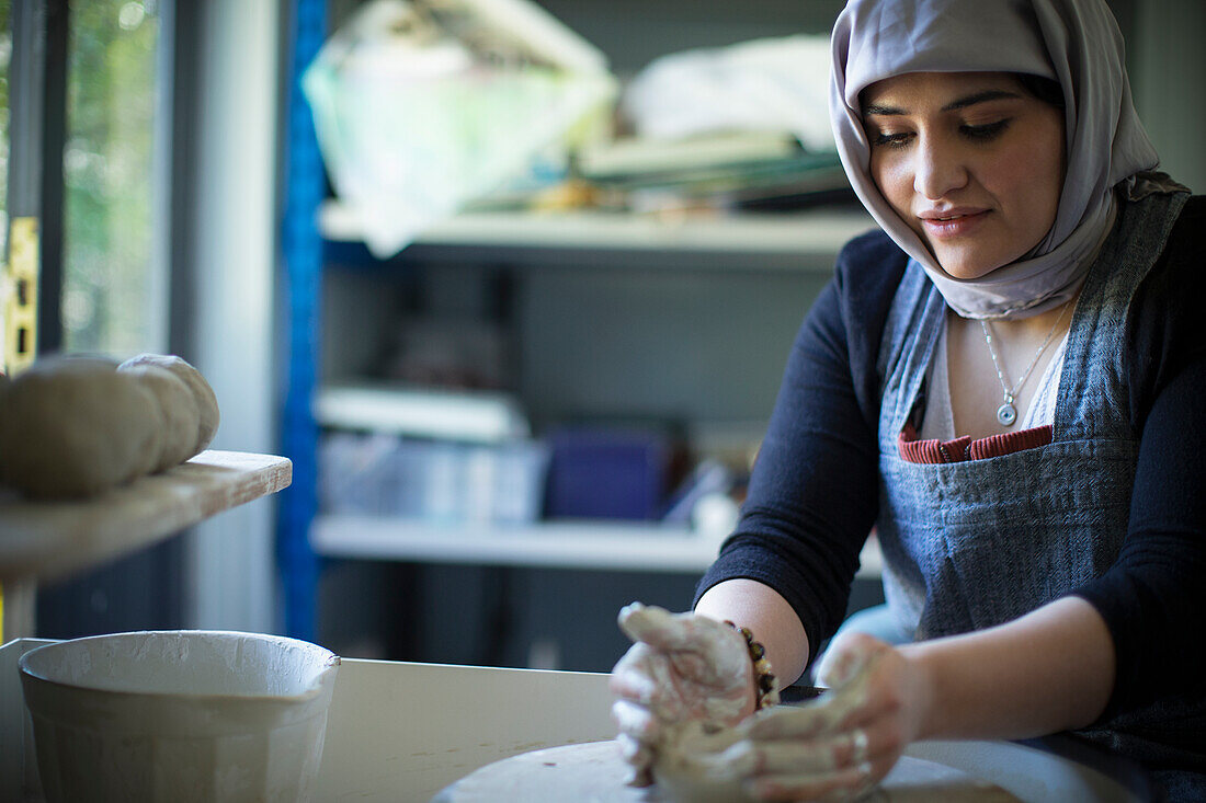 Young female Muslim artist at pottery wheel in art studio