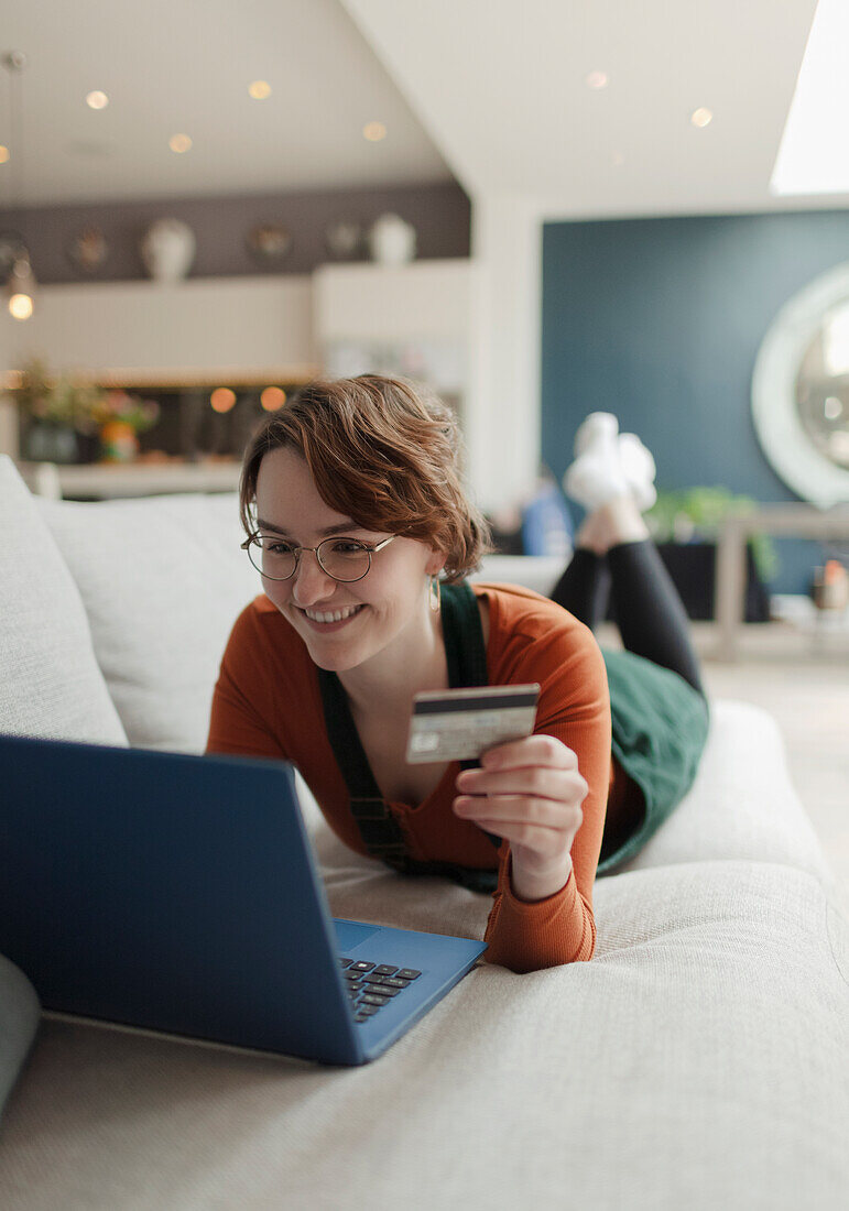 Happy woman with credit card online shopping at laptop on sofa