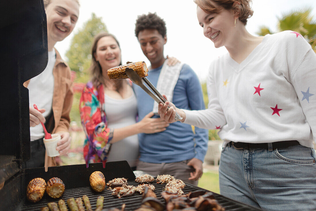 Happy friends barbecuing corn at barbecue grill