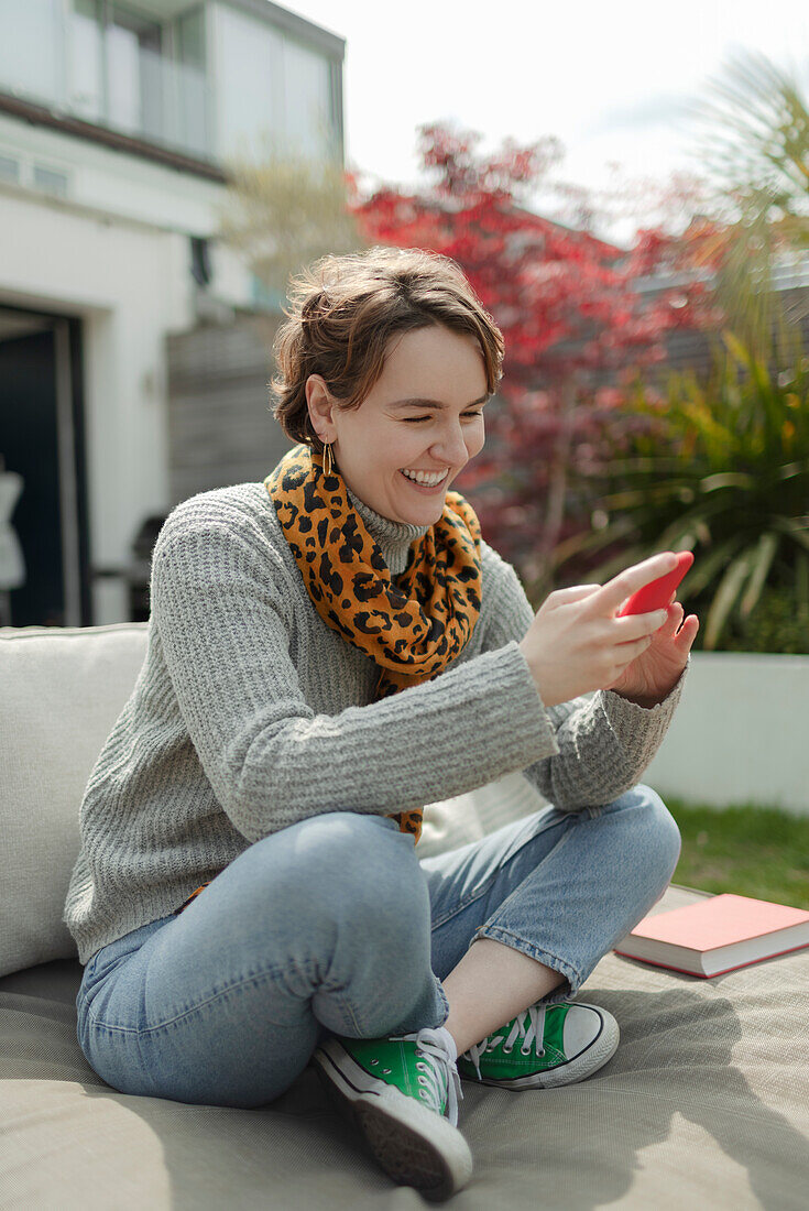 Happy woman using smart phone on sunny patio lounge chair