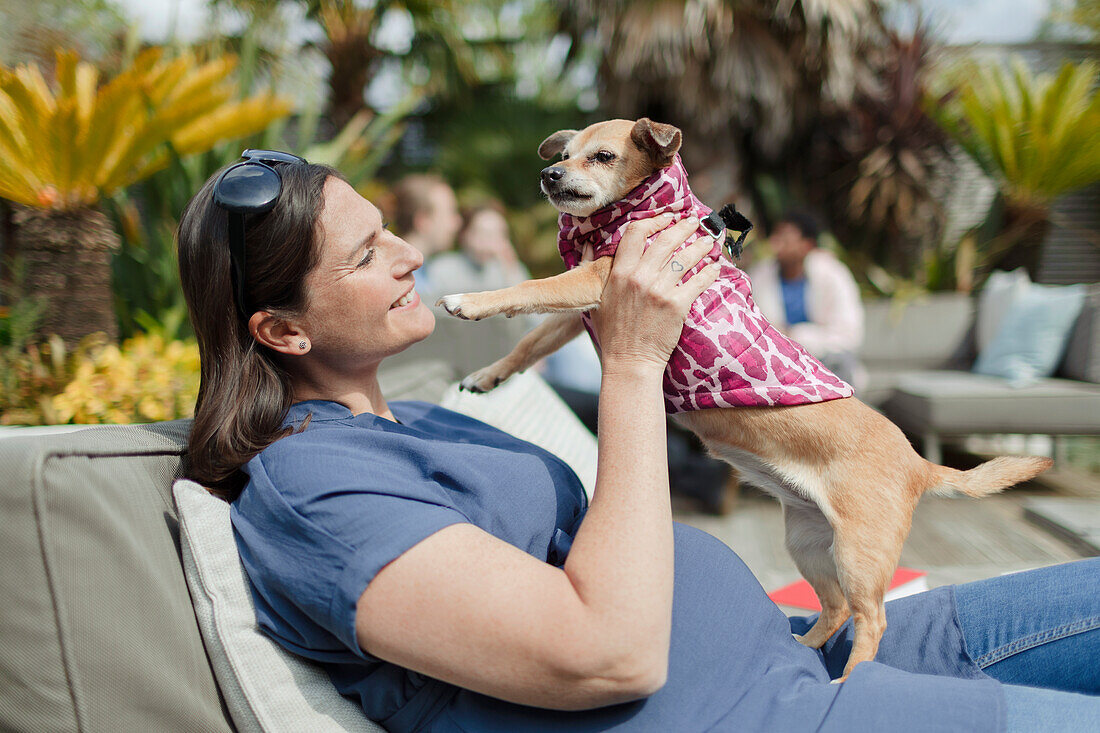 Happy pregnant woman with dog on sunny patio