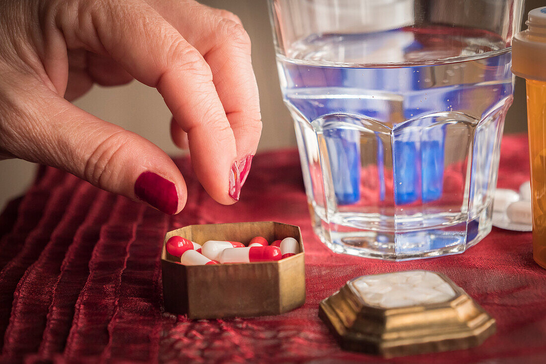 Woman taking a red and white pill from a pillbox