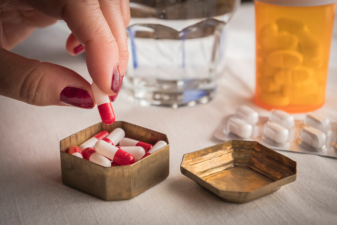 Woman taking a red and white pill from a pillbox