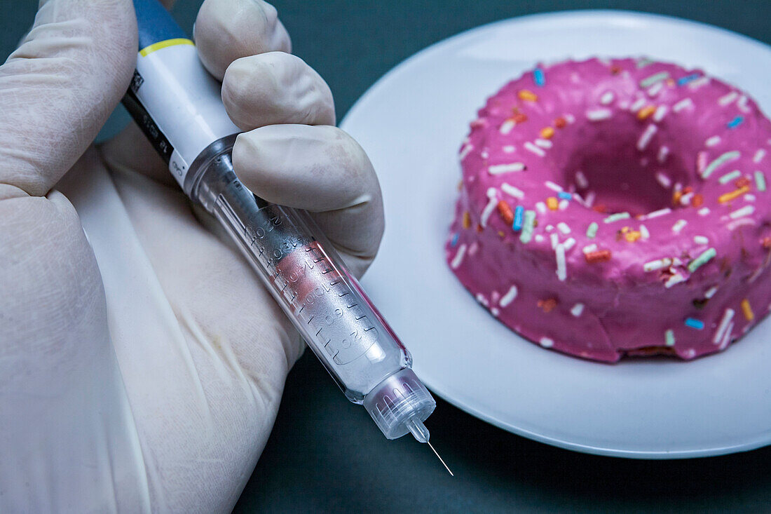 Hand holding an insulin pen next to a cake