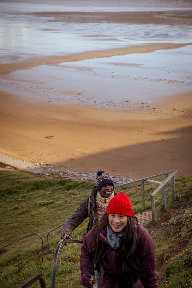 Happy couple hiking up steps over winter beach
