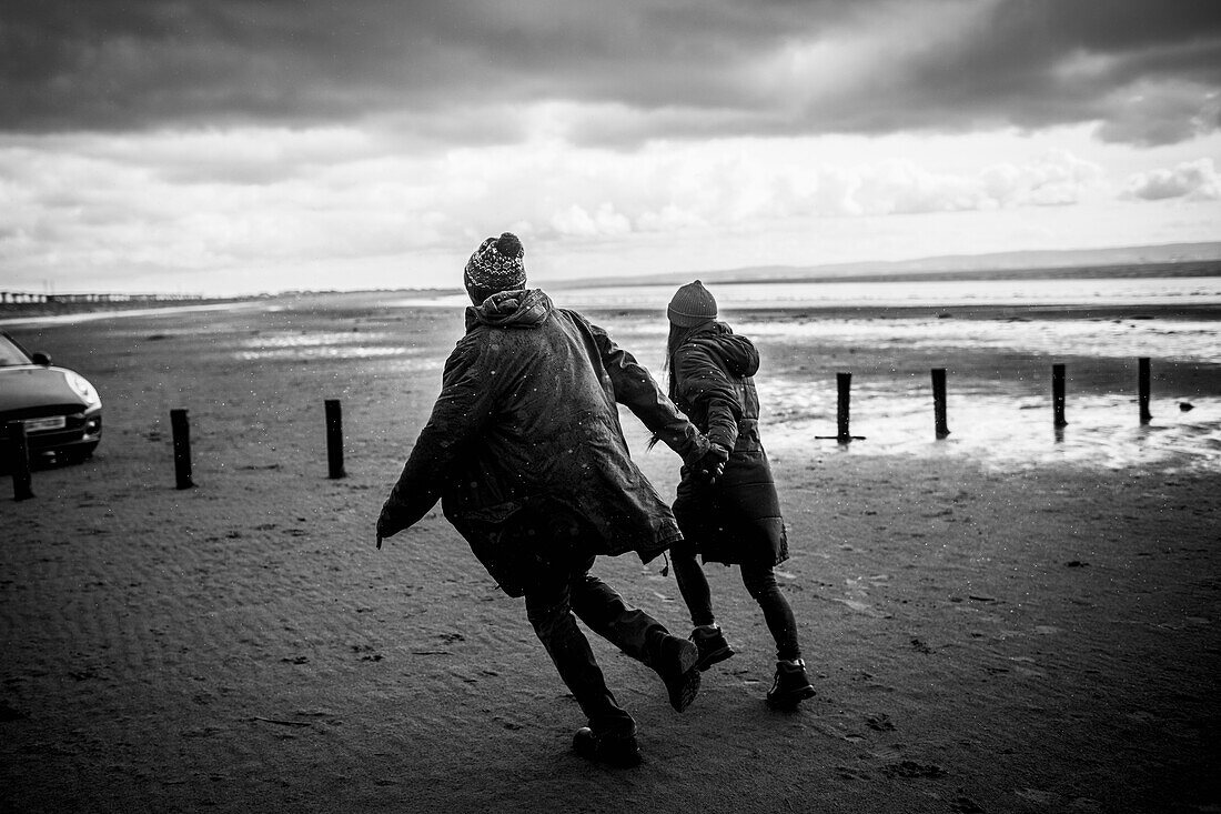 Couple holding hands running on winter beach