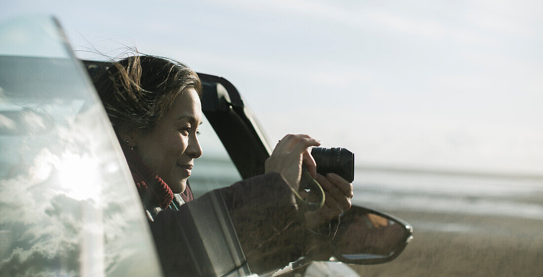 Woman with digital camera in convertible on winter beach