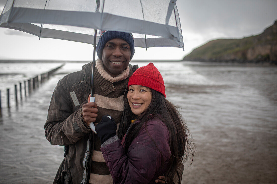 happy couple under umbrella on wet winter beach
