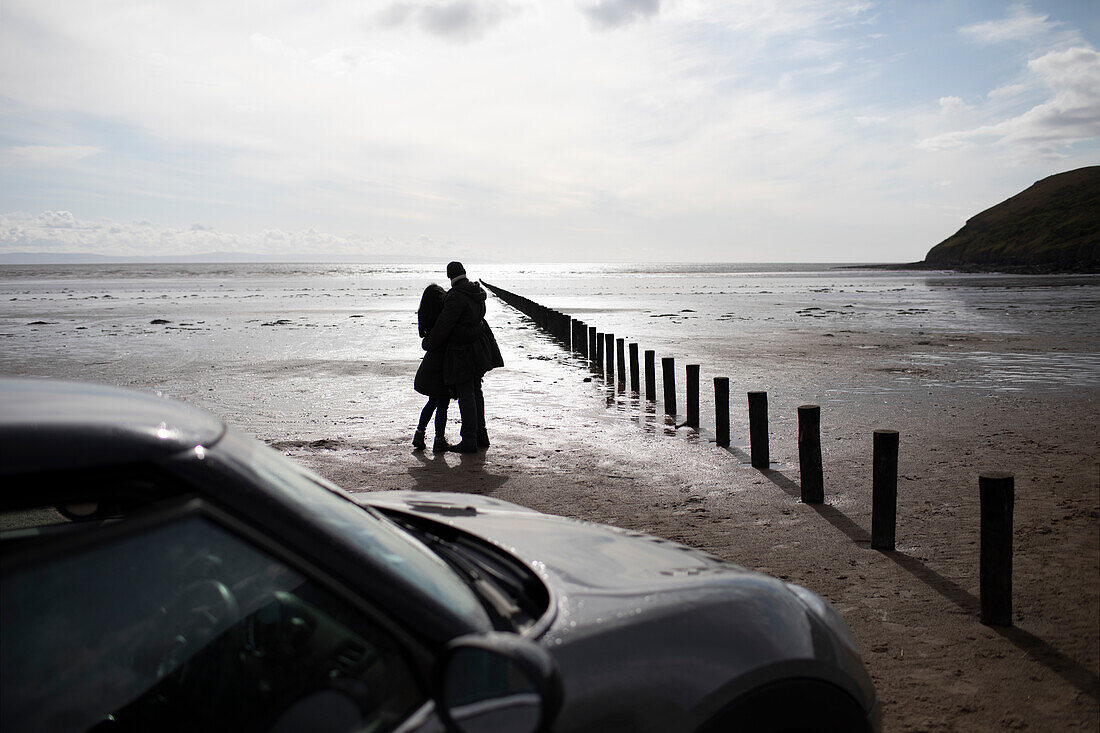 Silhouette of couple hugging on sunny wet winter beach