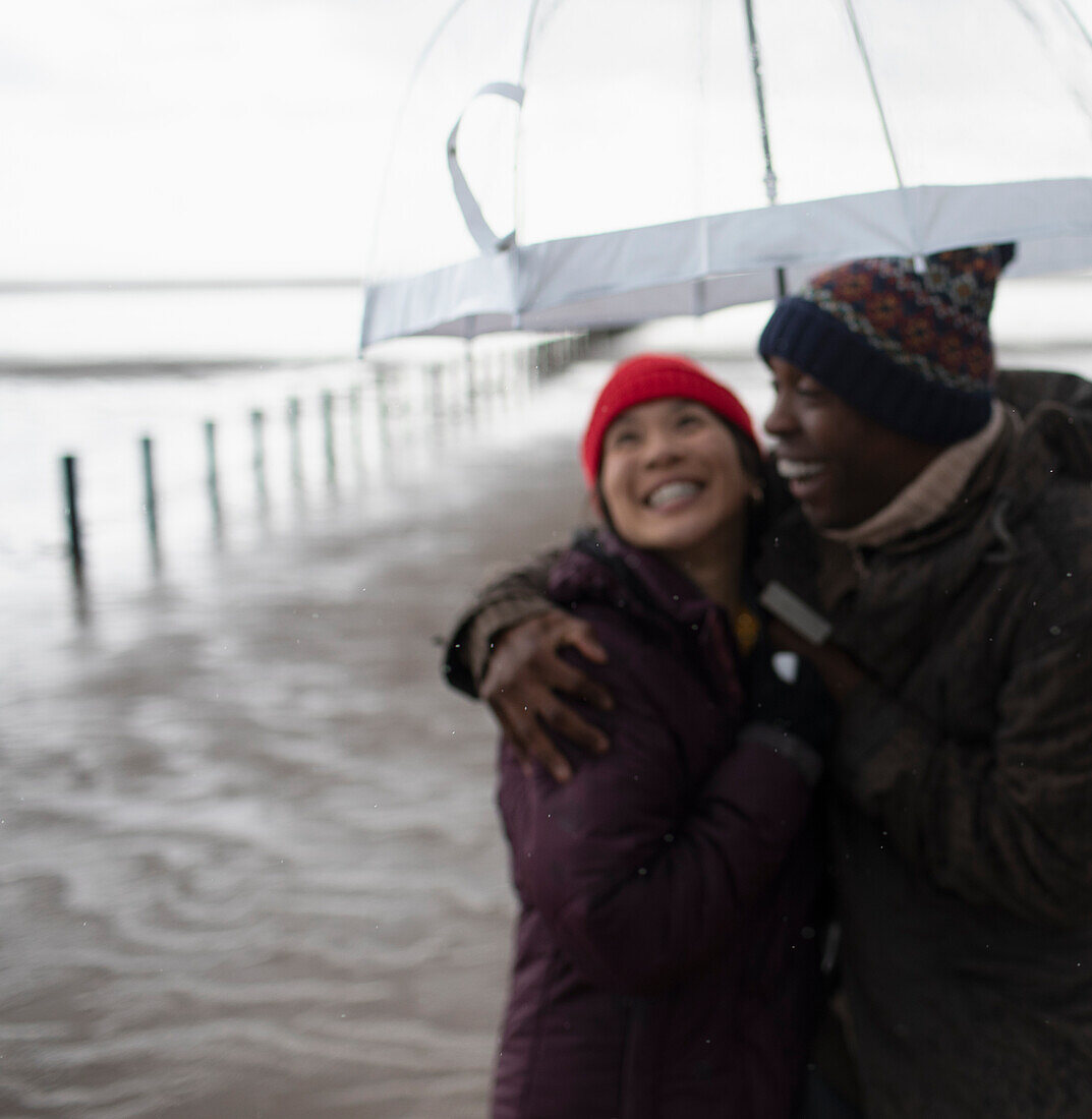 Happy couple in warm clothing under umbrella