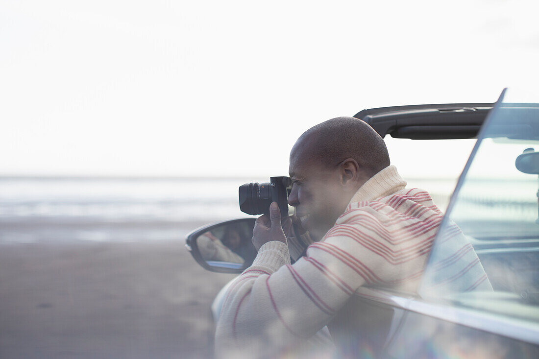 Man with digital camera in convertible on winter beach