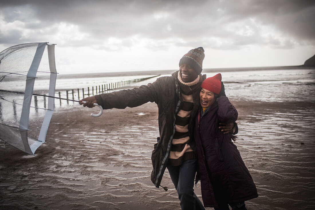 Affectionate couple with umbrella on wet winter beach